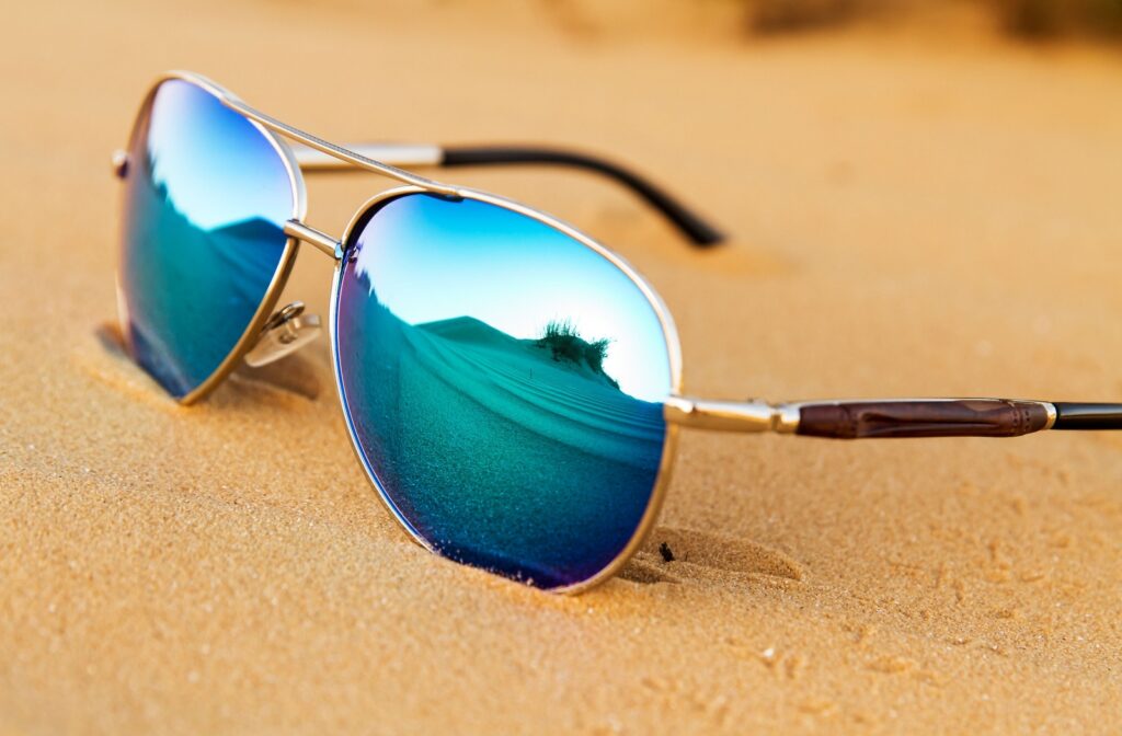 Close-up of a pair of blue polarized sunglasses placed on a sandy seashore.