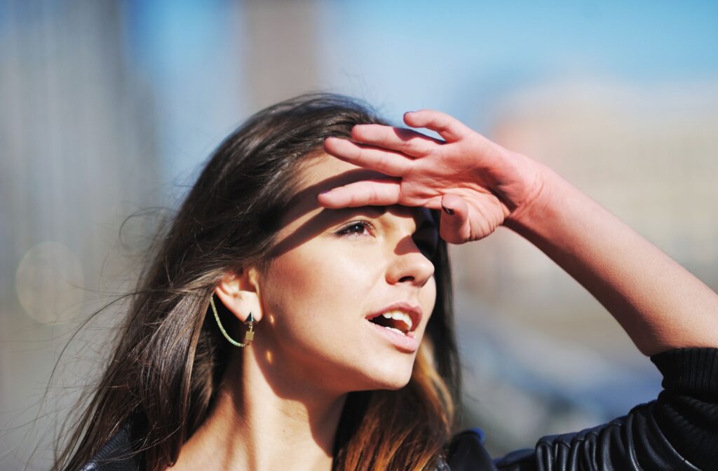 a woman is shading her eyes with her hands since the sun is so bright that it could cause and eyeball sunburn.