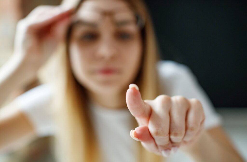 A blurry adult with blonde hair lifts their eyeglasses, pointing an in-focus finger straight ahead