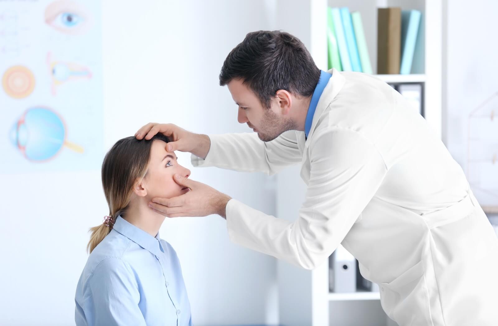 An eye doctor examining an adult patient's eye in a clinical setting.