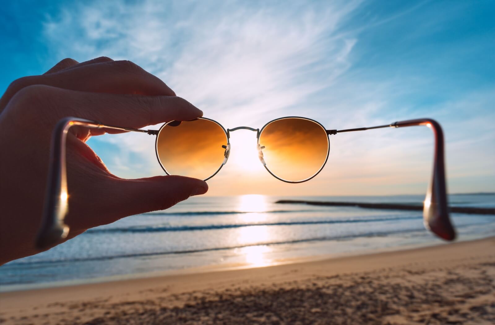 Sunglasses being held up to the sun at the beach.