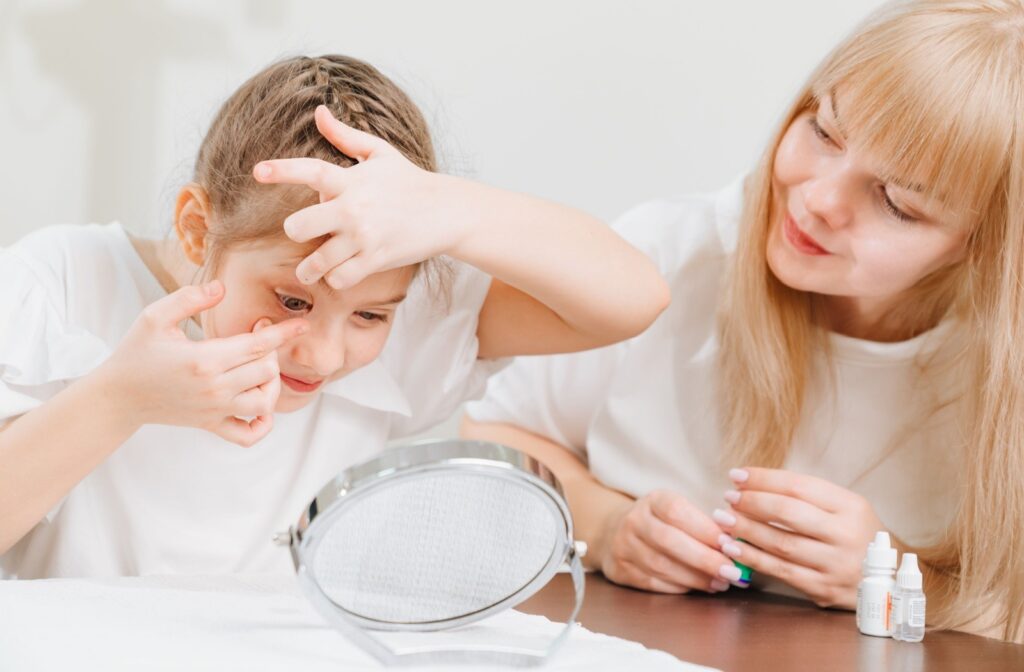 A young child putting in contact lenses with her parent beside her