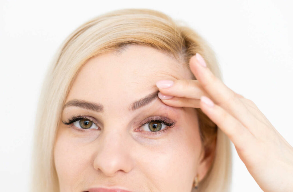A woman using her finger to raise her eyelid in an attempt to find a way to overcome droopy eyelid look.