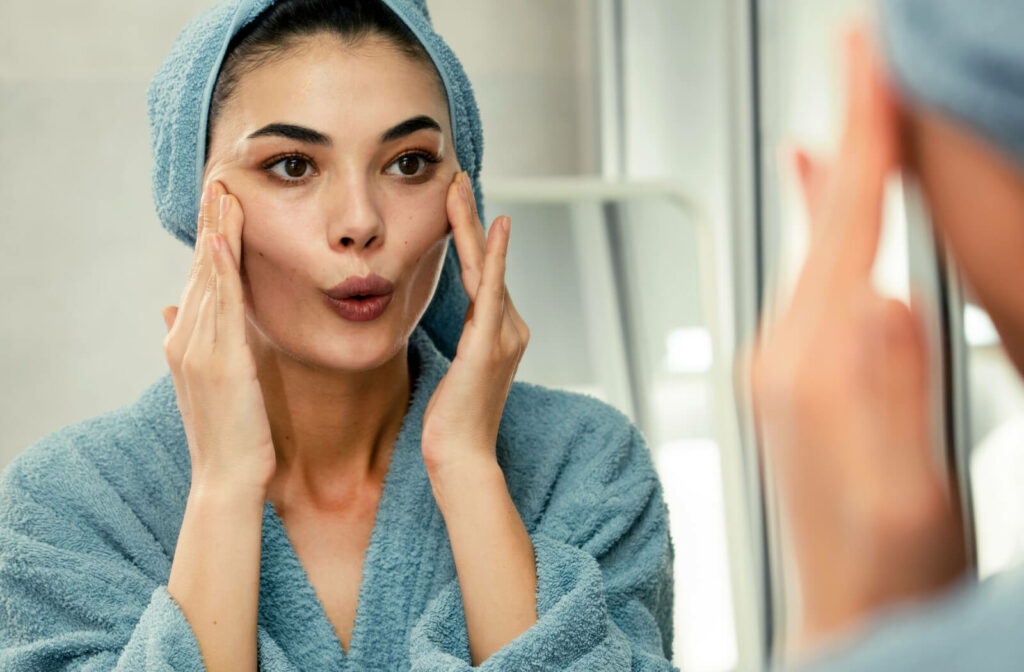 A close-up of a woman in the mirror is massaging her face and doing facial exercise.