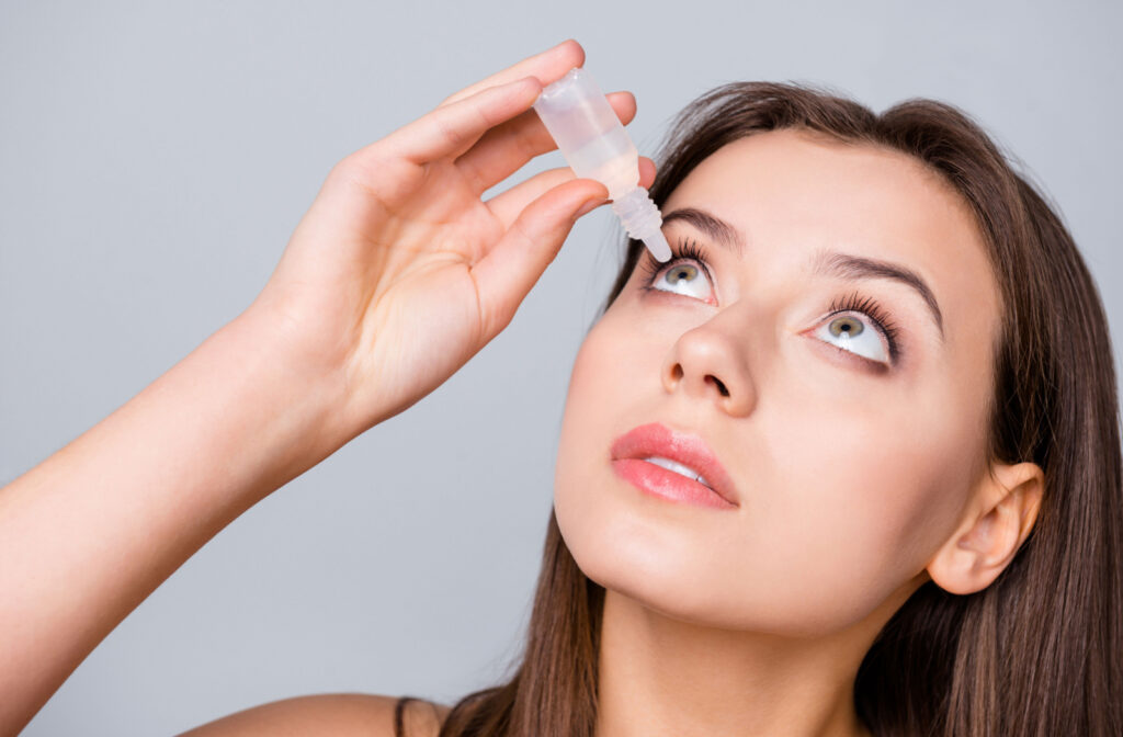 Close-up of a woman looking up while she applies eye drops in her right eye with her right hand.