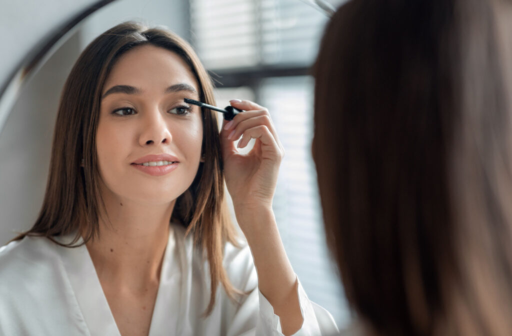 A woman applying mascara in the mirror.