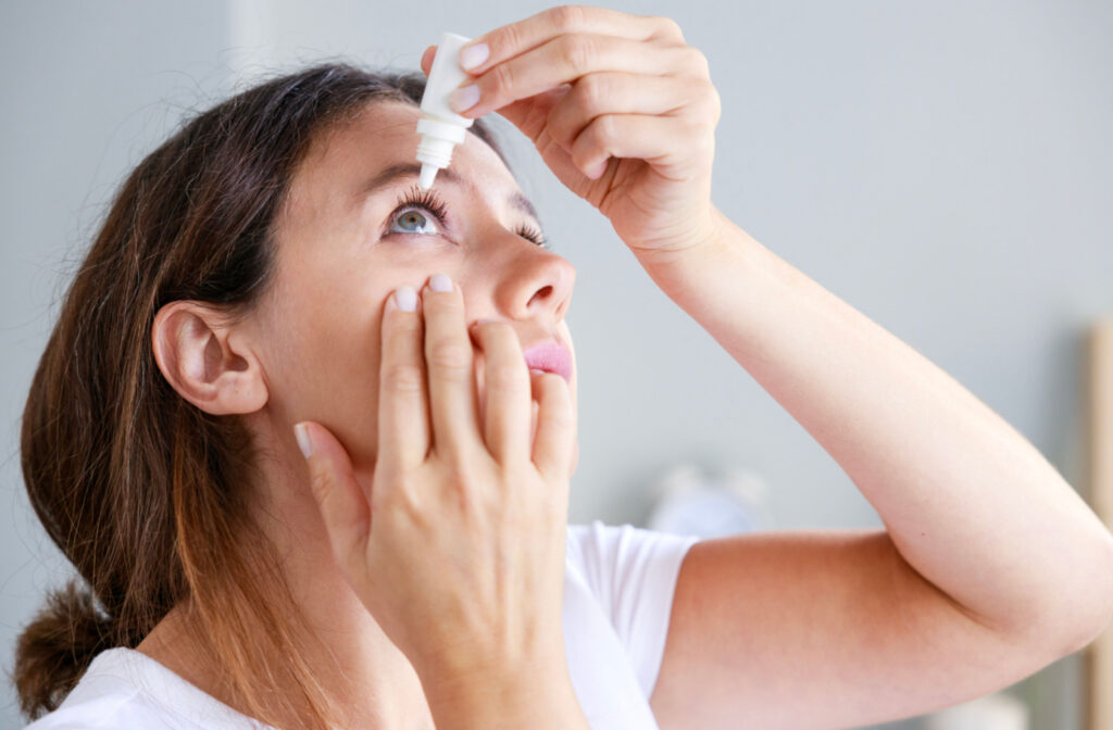 A woman putting eye drops with one hand while holding her cheek down with the other.
